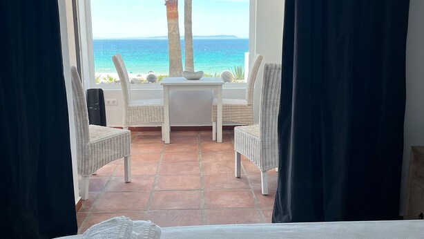 Una habitación con cama, una mesa y dos sillas frente a una vista al mar.