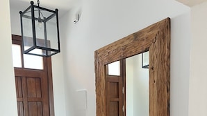 Un pasillo con una puerta de madera, un espejo grande con marco rústico y una lámpara colgante.