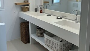 Un baño moderno con un tocador blanco, un espejo grande y estanterías integradas.