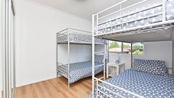 A dormitory room with bunk beds, a small desk, and a window.