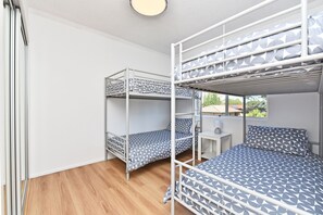 A dormitory room with bunk beds, a small desk, and a window.