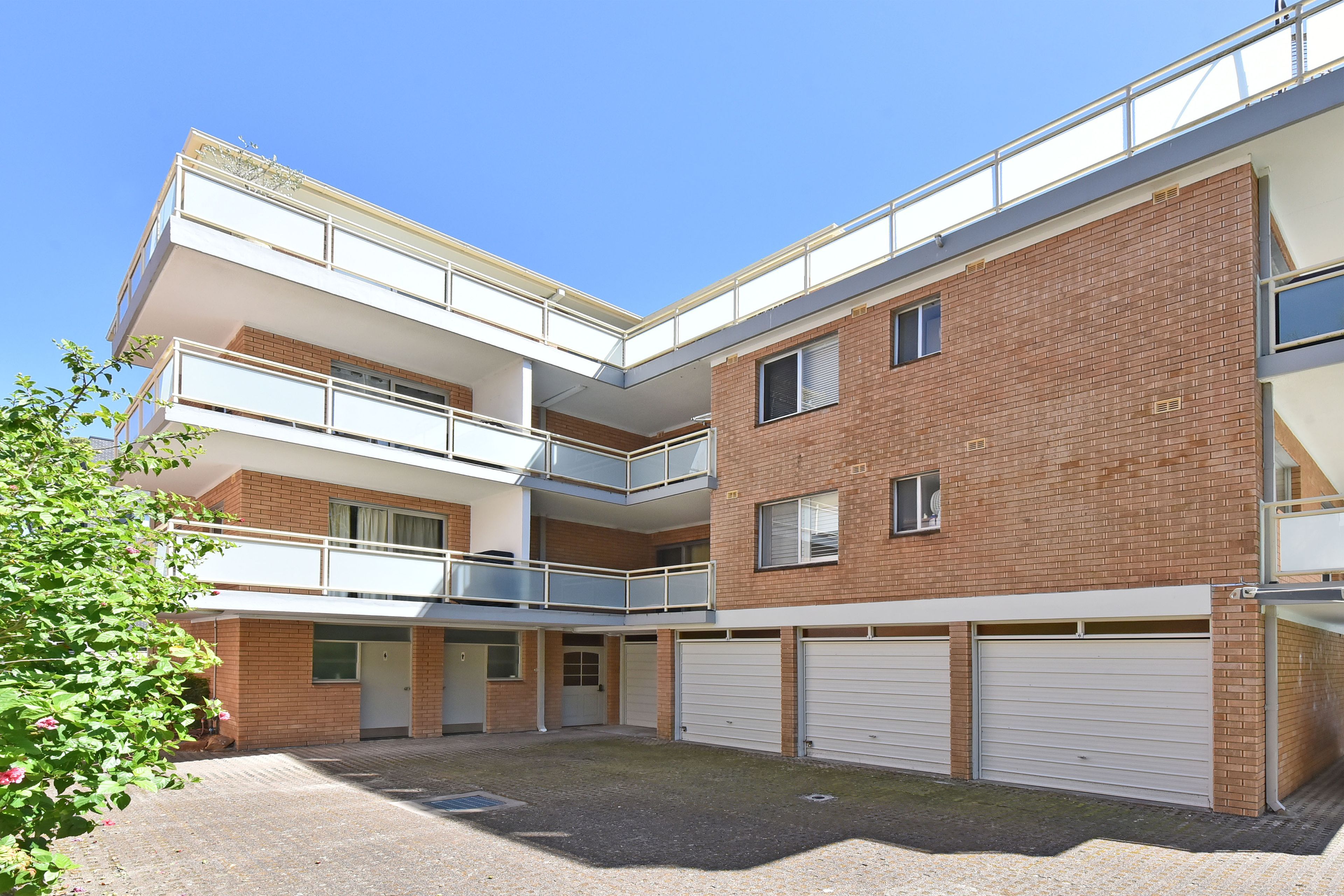 A multi-story building with a courtyard, featuring balconies, brick walls, and garage doors.