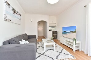 A living room with a grey sofa, a coffee table, and a TV displaying a beach scene.
