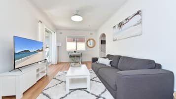 A modern living room with a flat-screen TV, grey sofa, white coffee table, and a patterned rug.
