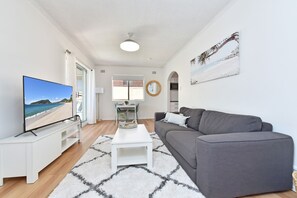 A modern living room with a flat-screen TV, grey sofa, white coffee table, and a patterned rug.