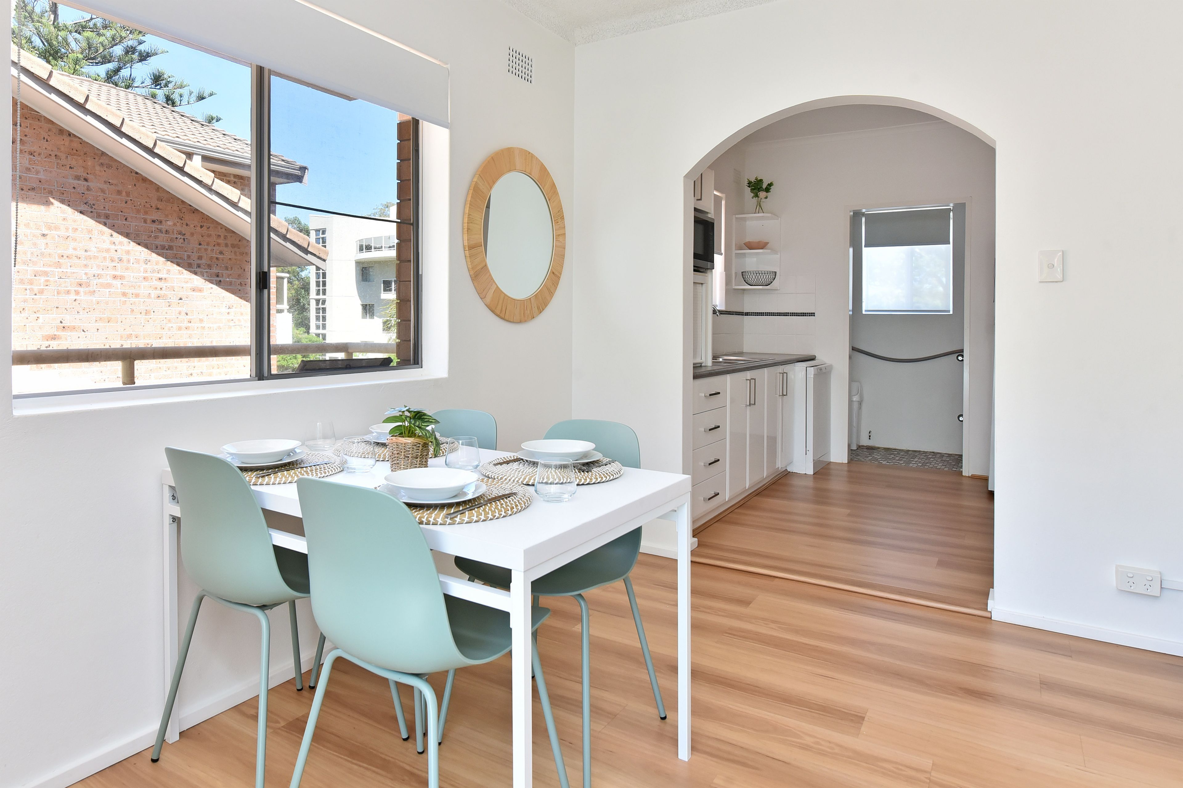 Comedor con una mesa blanca, sillas color turquesa y vista a un edificio de ladrillo.