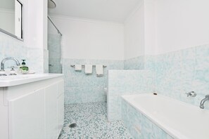 Een badkamer met een wit wastafel, een spiegel, een douche en een bad.