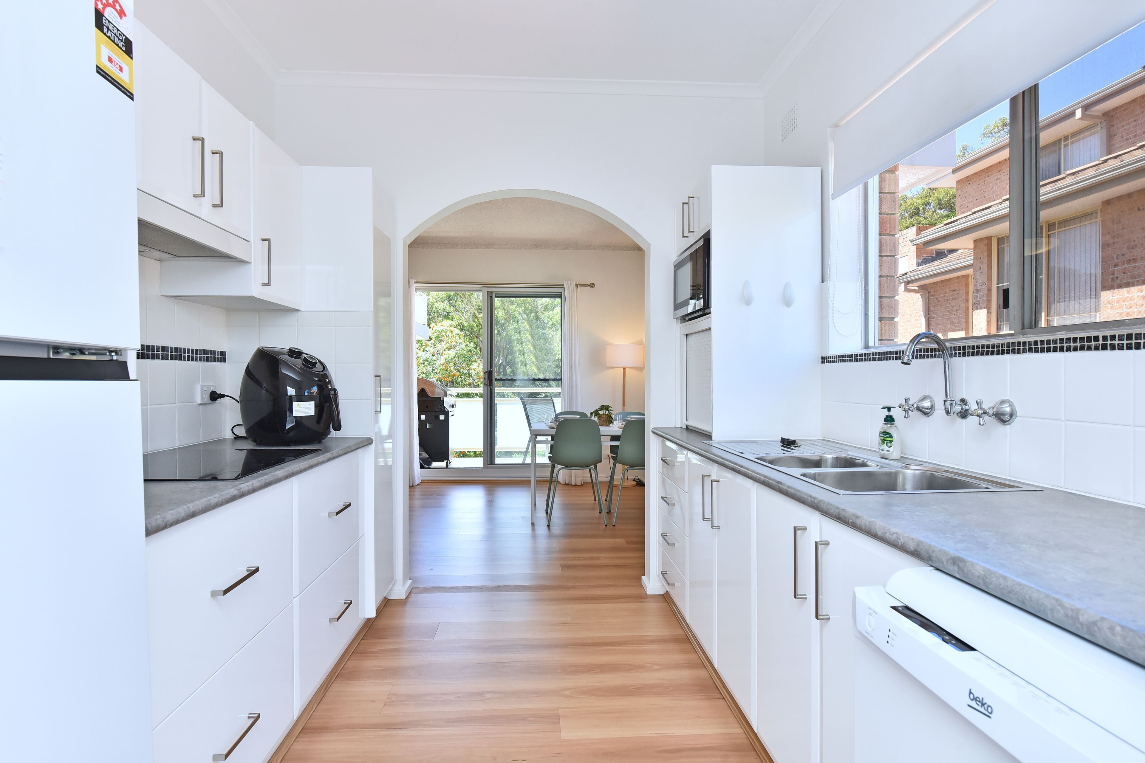 A modern kitchen with white cabinetry, a built-in microwave, and a large window.