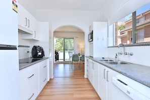 A modern kitchen with white cabinetry, a built-in microwave, and a large window.