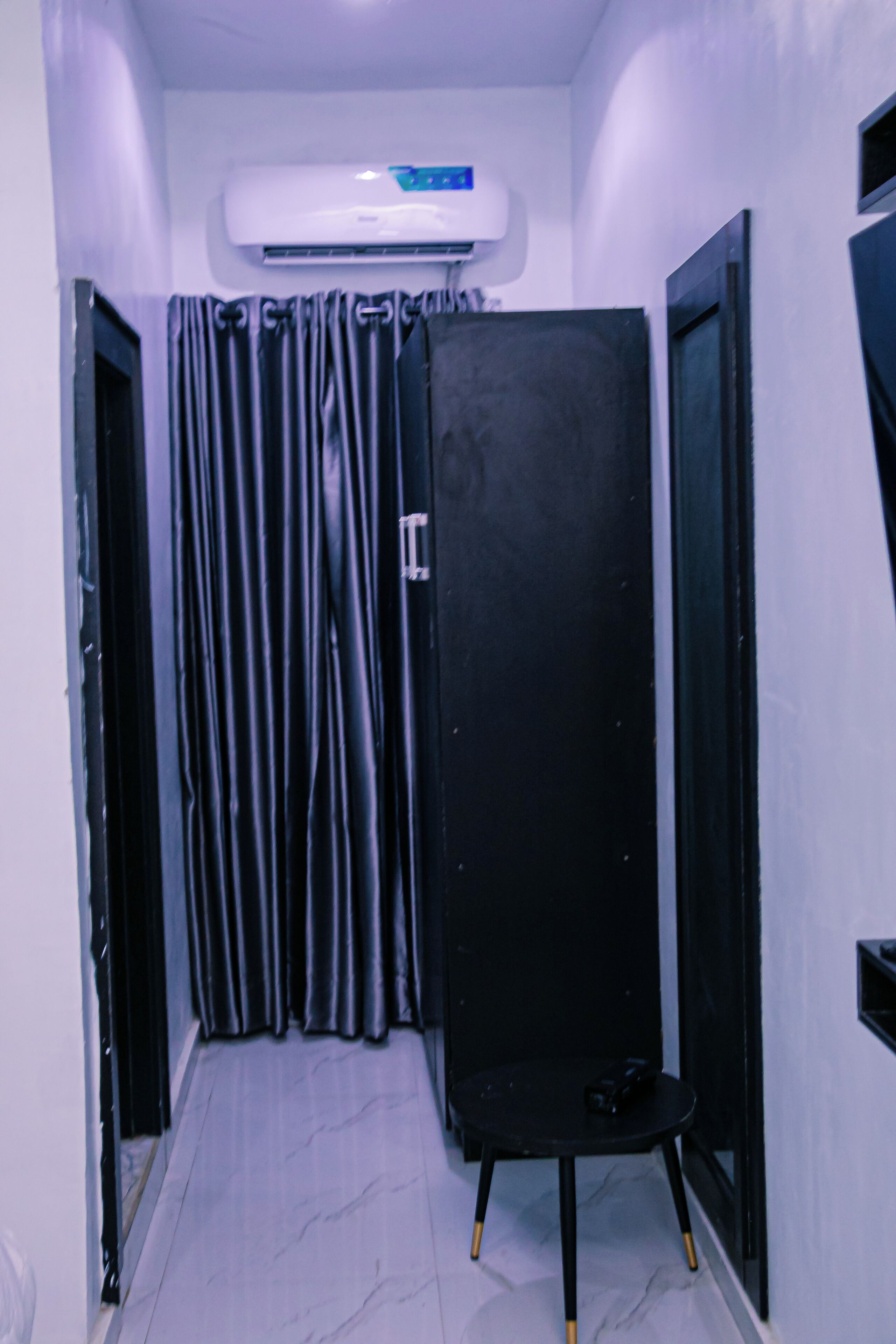 Un couloir étroit avec un meuble noir, une chaise noire et un rideau.