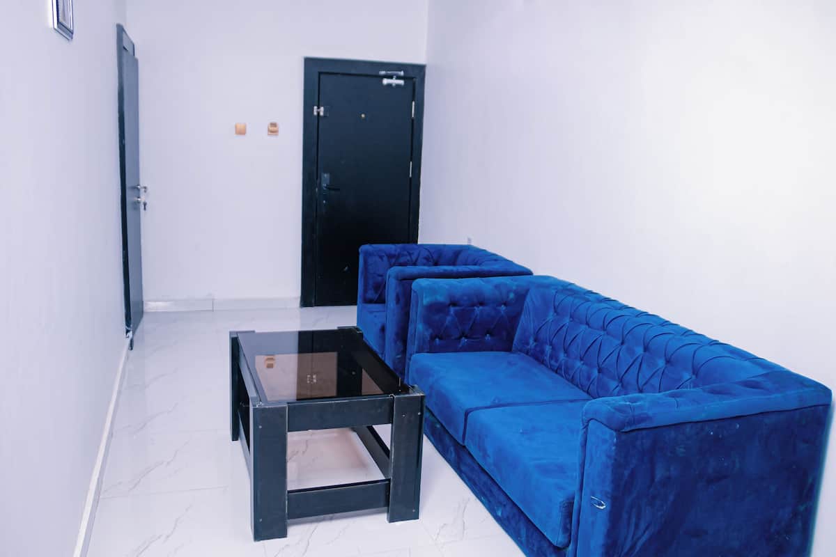 Ein Zimmer mit einem blauen Sofa, einem Glastisch und einer schwarzen Tür.