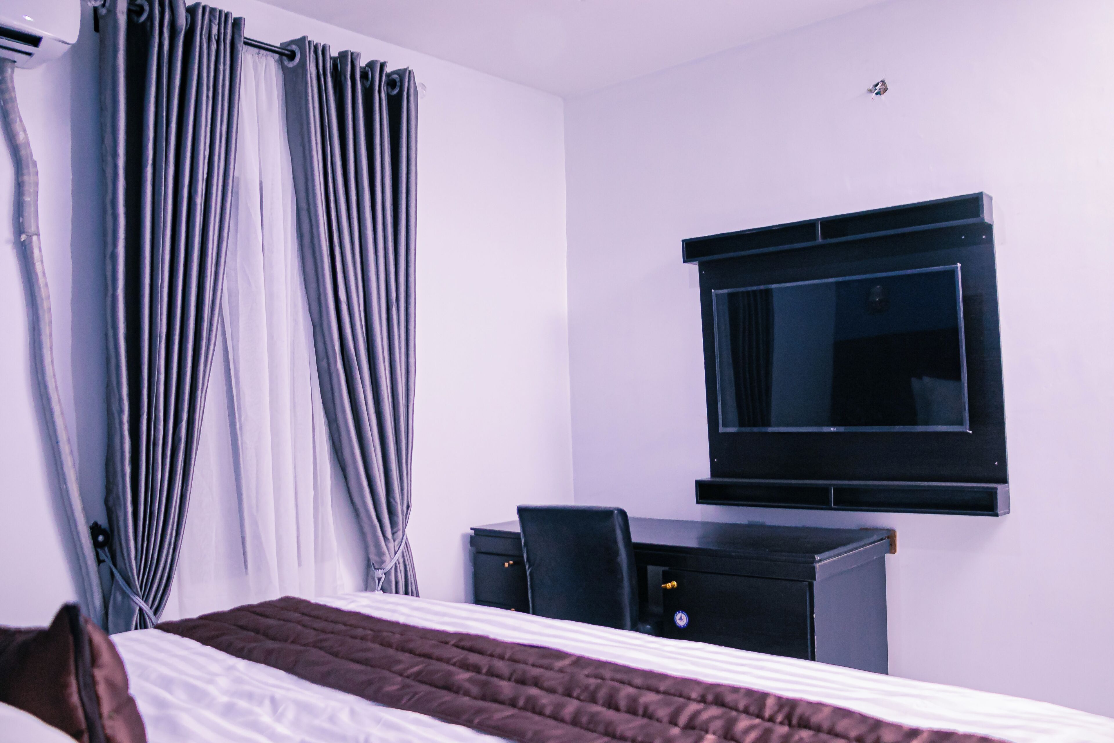 A hotel room with a bed, a desk, a chair, a TV, and curtains.