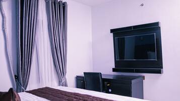 A hotel room with a bed, a desk, a chair, a TV, and curtains.