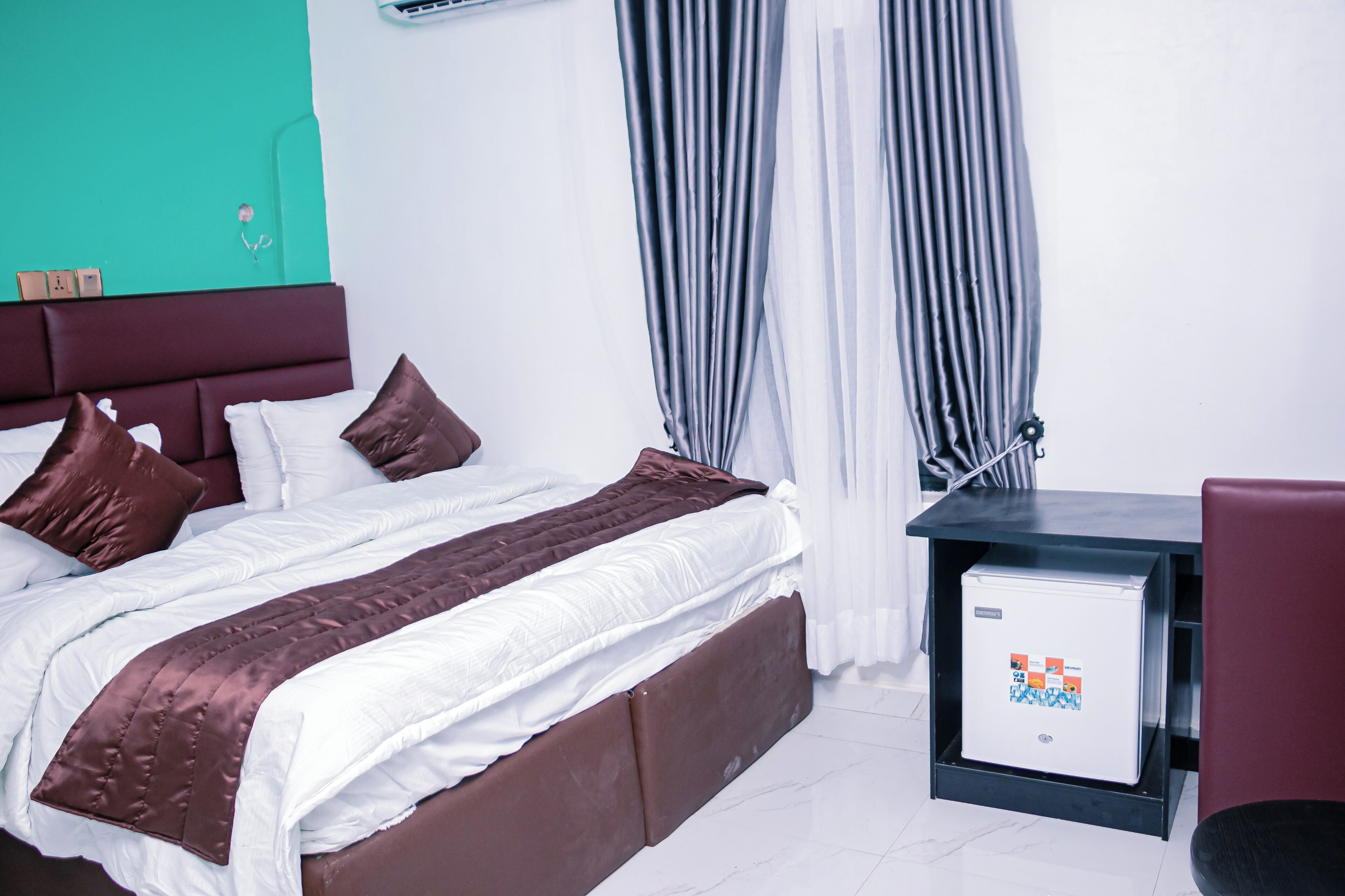 A hotel room with a bed, a desk, and a refrigerator.