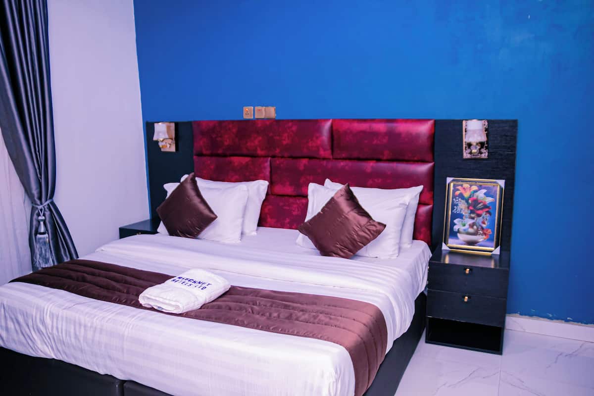 Ein Hotelzimmer mit einem großen Bett, einem Nachttisch mit einem gerahmten Bild und einer blauen Wand.
