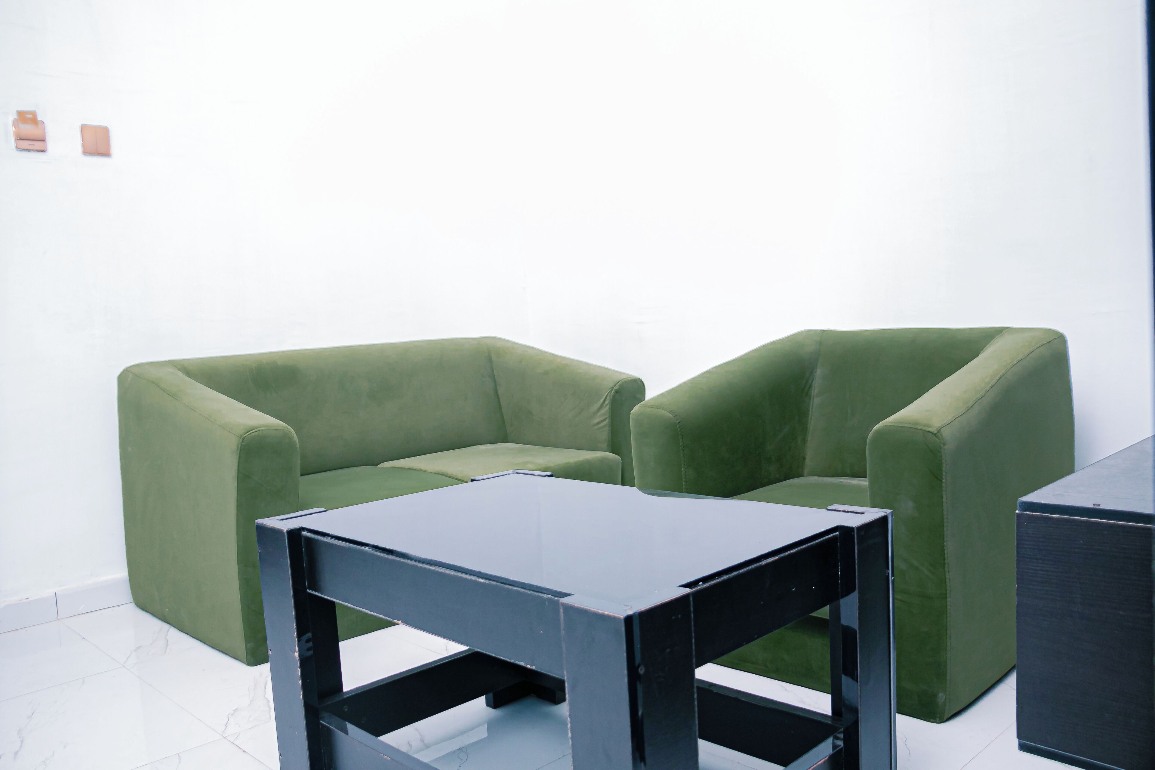 Een kamer met twee groene fauteuils en een zwarte tafel.