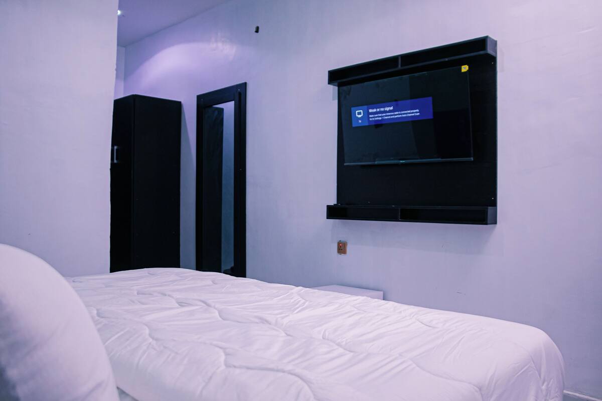 Ein Hotelzimmer mit einem Bett, einem an der Wand befestigten Fernseher und einer Tür.