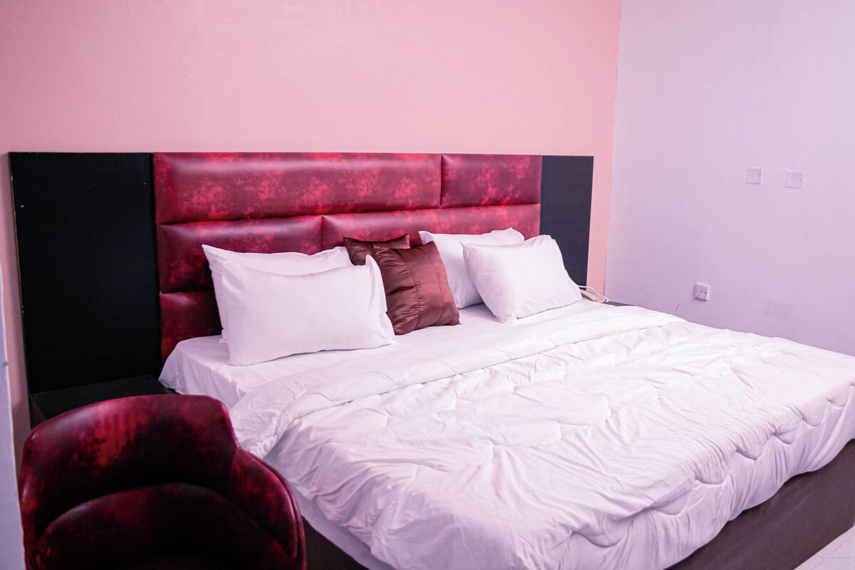 Ein Bett mit weißer Bettwäsche und einem roten Kopfteil, ein roter Sessel und eine schlichte Wand.