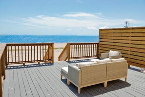 A wooden deck with a wicker sofa and a small table, overlooking a beach with a clear blue sky. - NEW! The Salt & Sun Beachfront Studio (Corpus Christi)