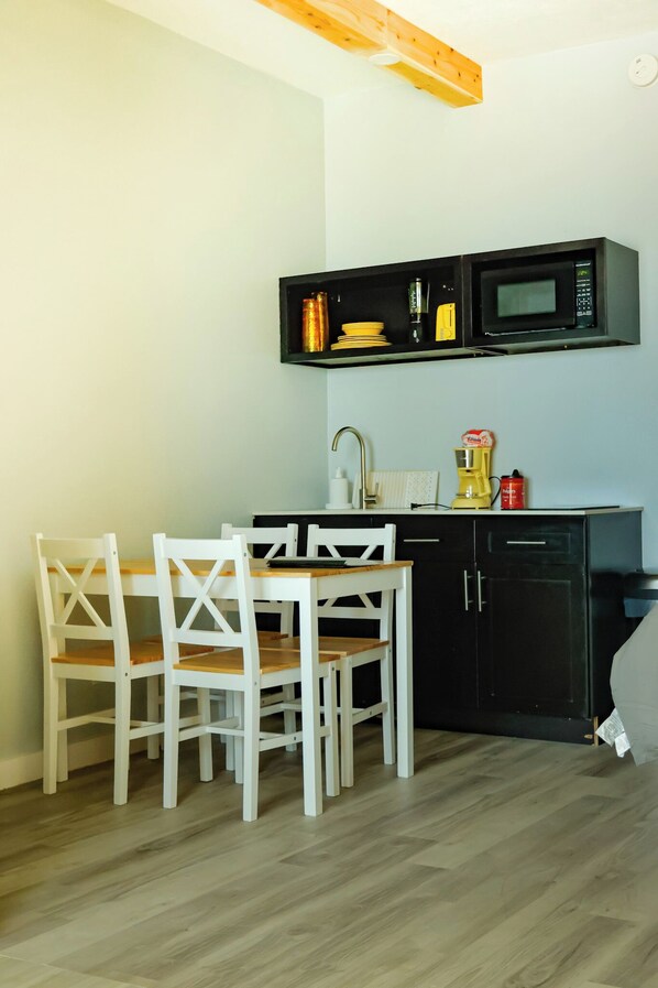 A small kitchen with a microwave, sink, and a white dining table with chairs. - NEW! The Salt & Sun Beachfront Studio (Corpus Christi)