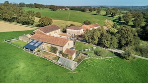 Una tenuta rurale con una grande casa, una serra e campi verdi circostanti.