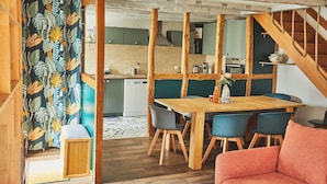 Zona pranzo con tavolo e sedie in legno, cucina sullo sfondo e una scala.