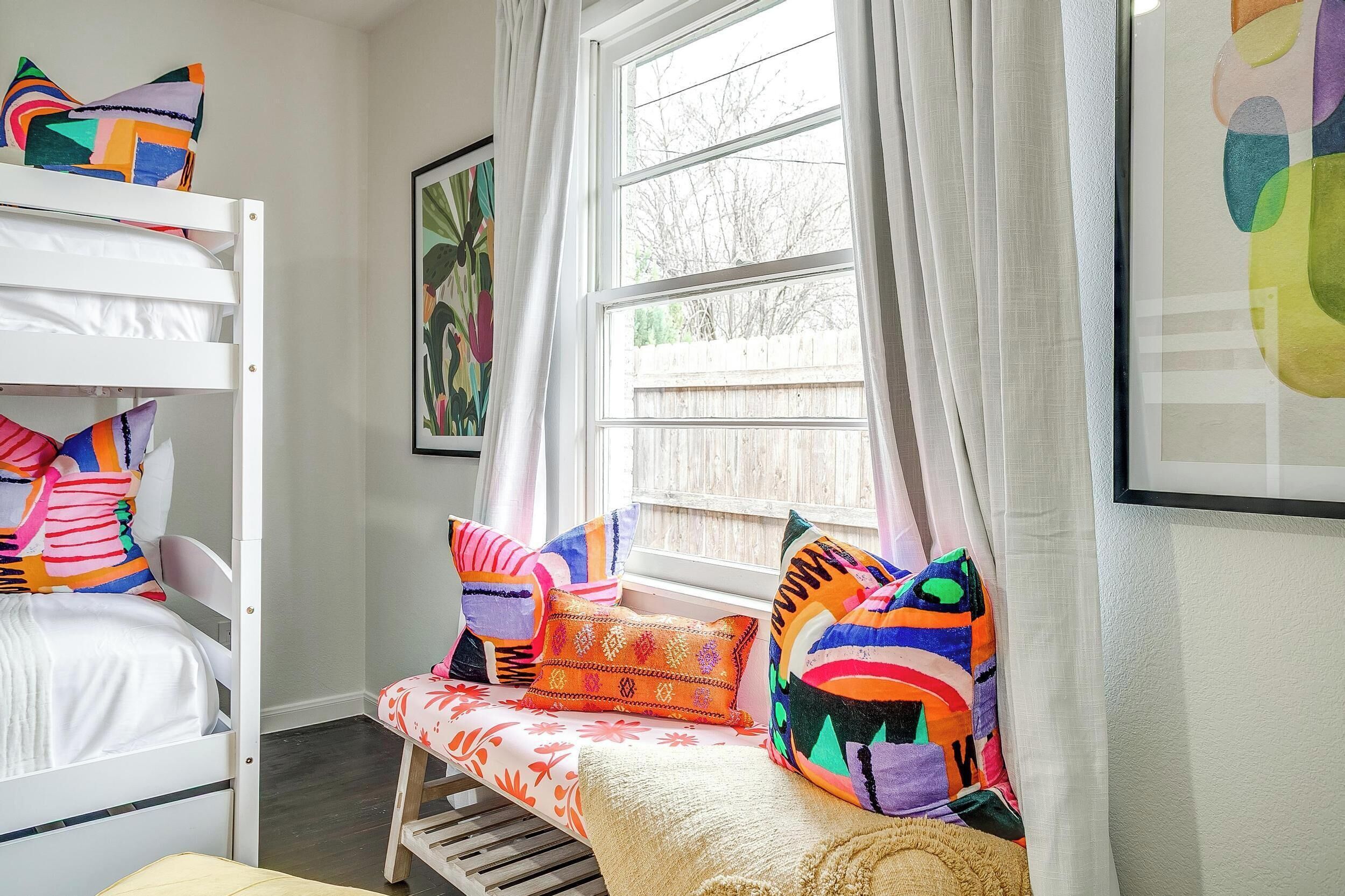 A bunk bed room with colorful pillows and a window with curtains.