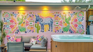 A patio area with a colorful mural, a sofa, a chair, and a hot tub. - Private Pool Oasis | Spa & Game Room • 12 (Fort Worth)