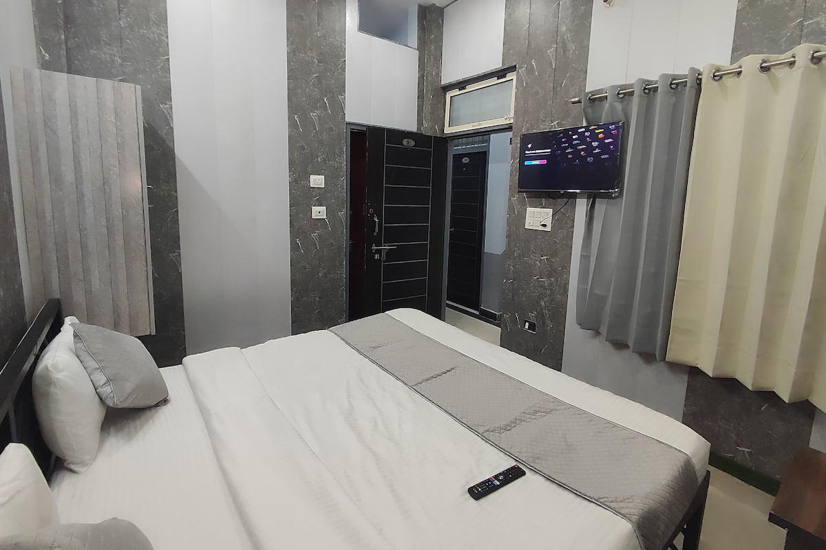 A modern bedroom with a bed, a TV mounted on the wall, and a door with a security lock.