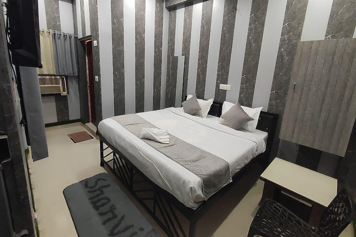 A modern bedroom with a large bed, striped walls, and a bedside table.