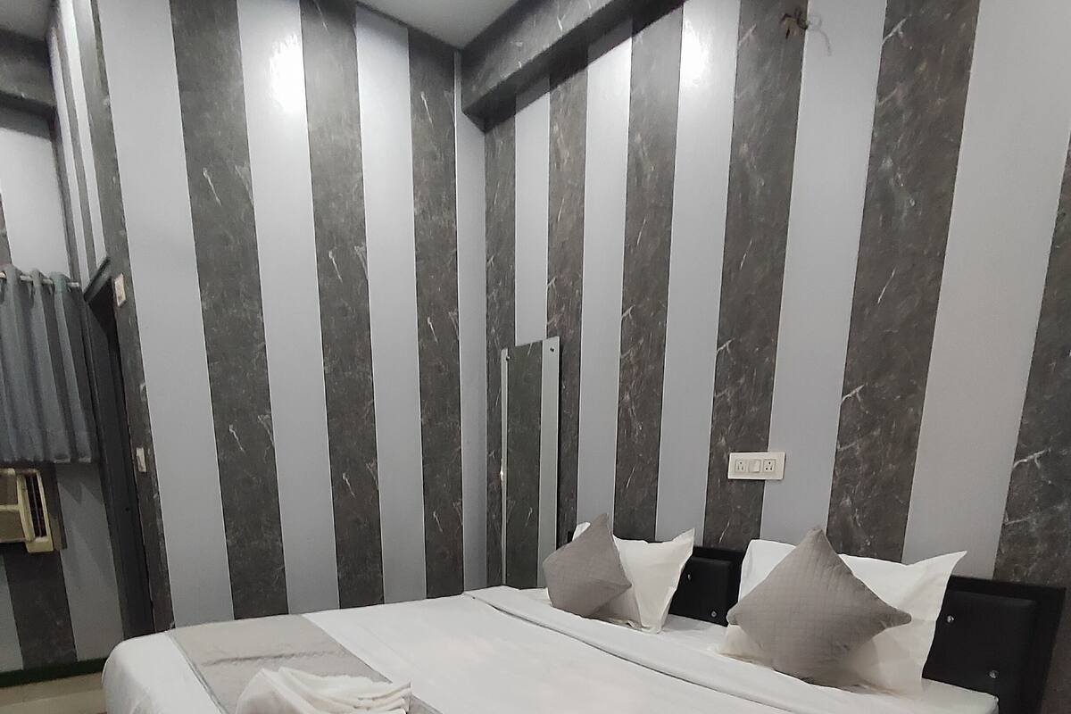 A modern hotel room with a large bed, grey and white striped walls, and a ceiling light.