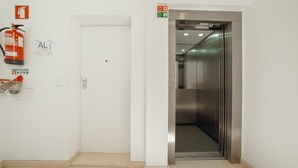 Un ascenseur propre et moderne, avec un intérieur métallique et une porte blanche. Un extincteur est fixé au mur, à côté de la porte.
