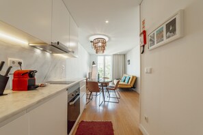 A modern kitchen with a built-in oven, a red coffee machine, and a dining area with a round table and chairs.