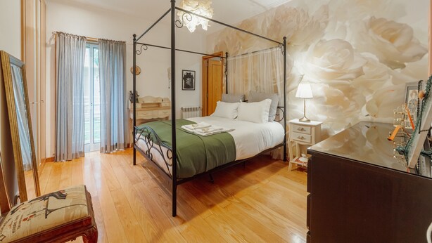 Una cama con dosel con una colcha verde, una mesita de noche con una lámpara y un gran mural floral en la pared.