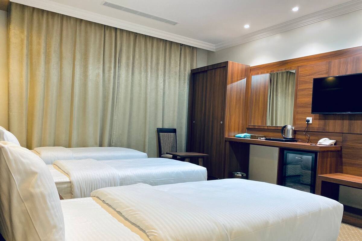 Una habitación de hotel con dos camas, un armario de madera, un escritorio con televisor y un minibar.