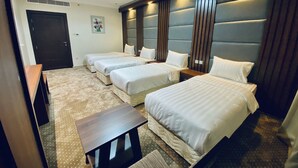 A hotel room with four single beds, a small wooden table, and a large window with a view.
