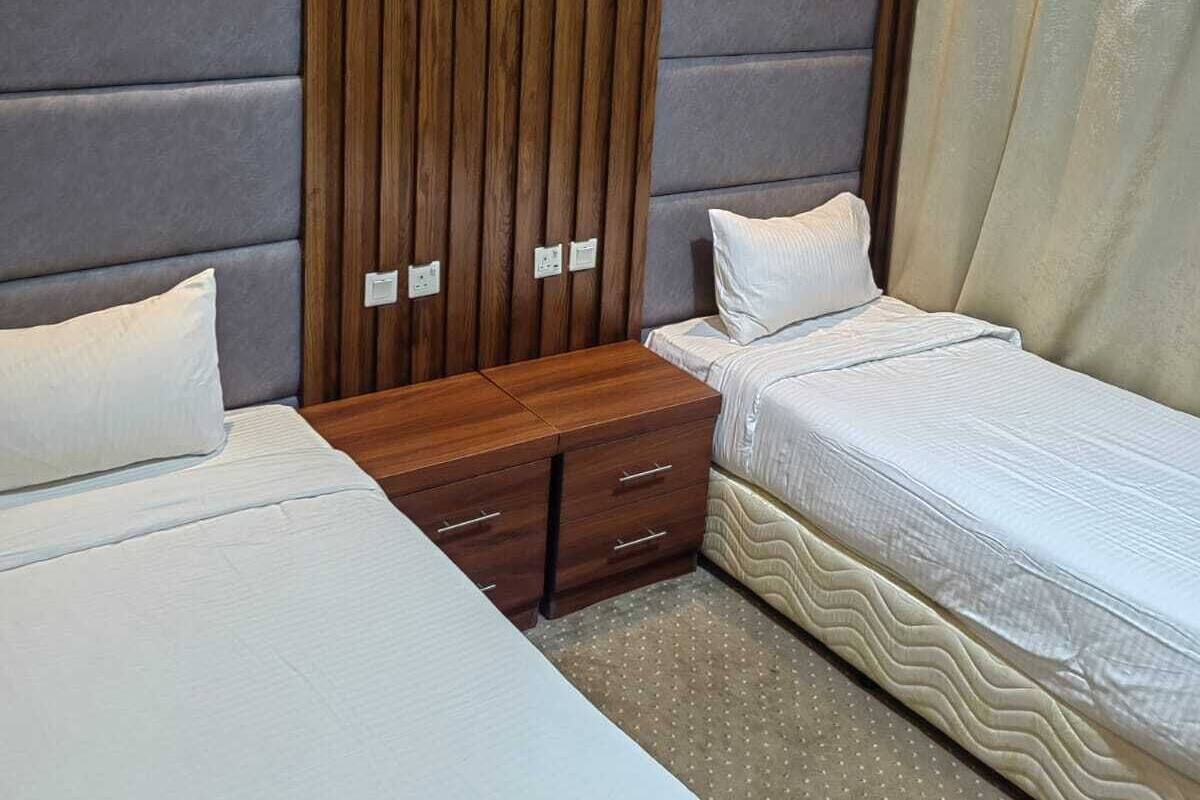 Una habitación de hotel con dos camas, un armario de madera y un ventanal con cortinas.