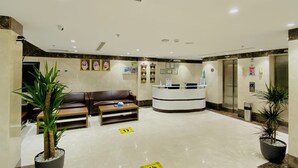 A reception area with a reception desk, a brown leather sofa, two potted plants, and a tiled floor with directional signs.