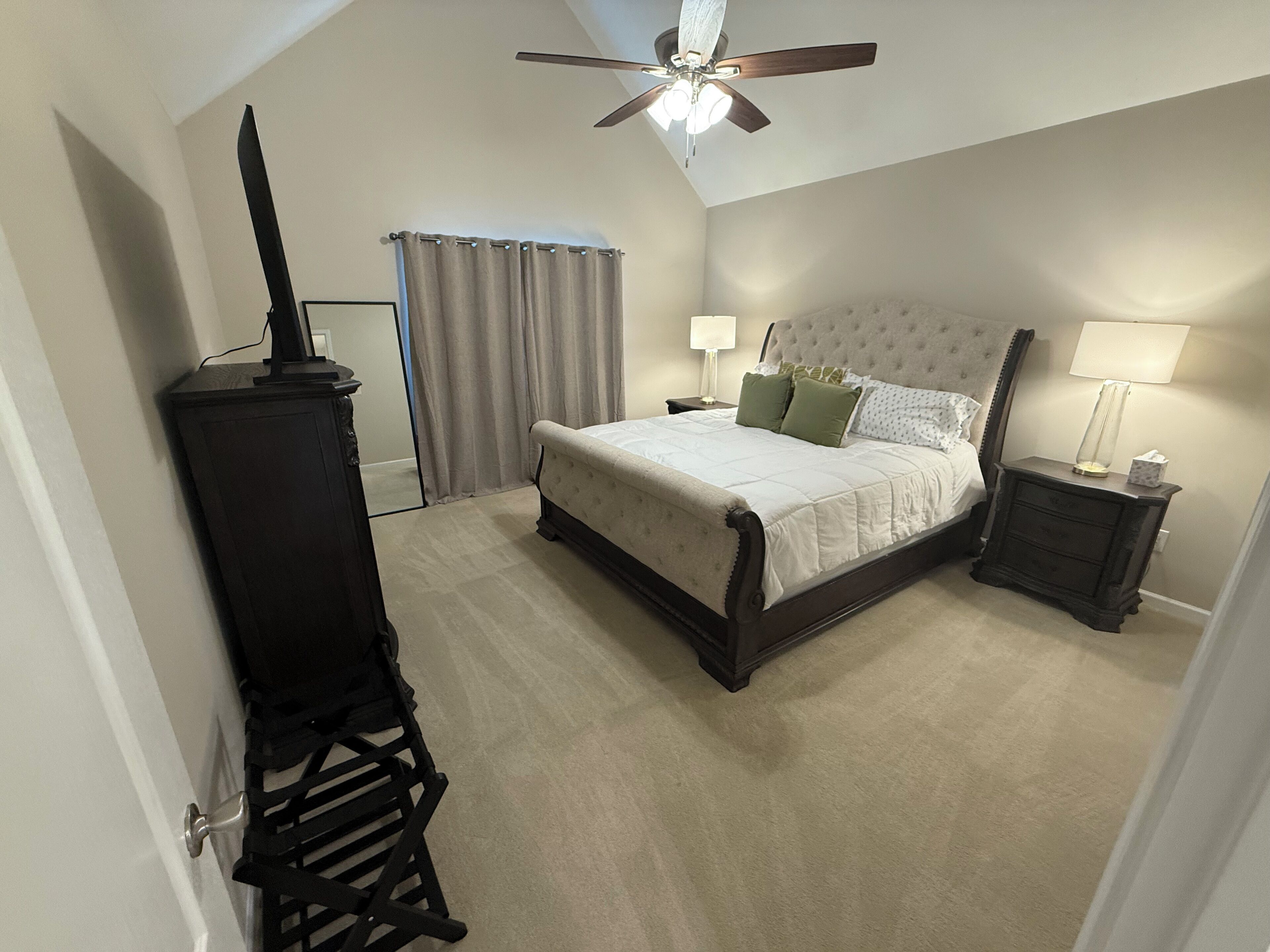 Une chambre à coucher avec un lit, des tables de chevet, un ventilateur de plafond et une fenêtre avec des rideaux.