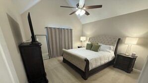 Ein Schlafzimmer mit einem Bett, Nachttischen, einem Deckenventilator und einem Fenster mit Vorhängen.