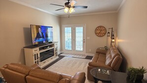 Ein Wohnzimmer mit Fernseher, zwei Ledersofas, einem Couchtisch, einem Deckenventilator und einer Wanduhr.