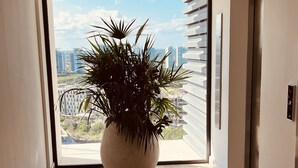 Un couloir agrémenté d’une grande plante en pot, une porte-fenêtre coulissante donnant sur un balcon et un ascenseur moderne.