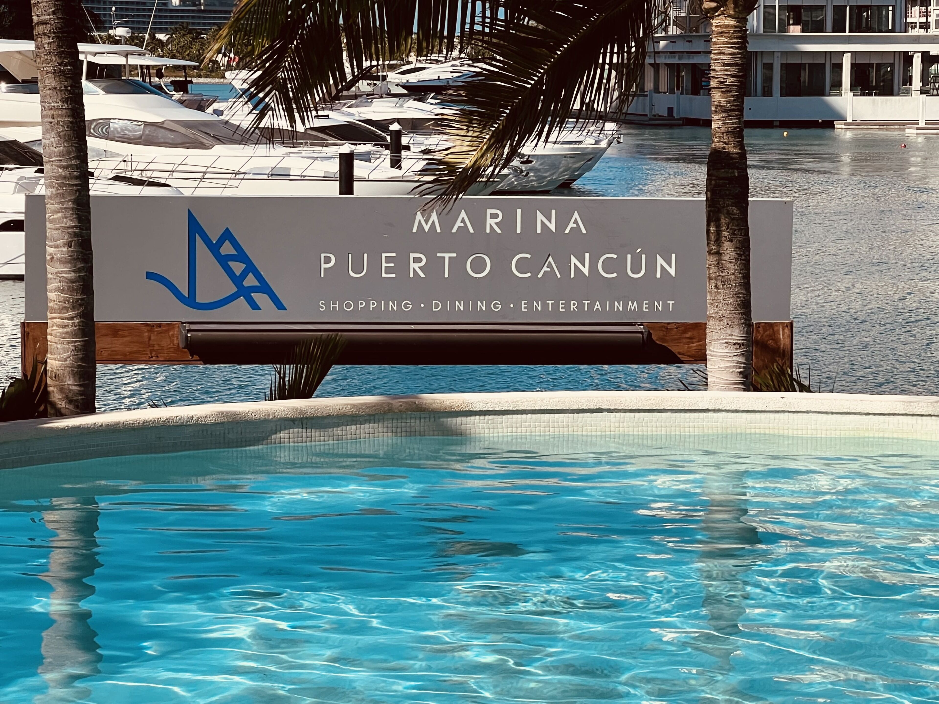 Señal de 'Marina Puerto Cancun' con una piscina y palmeras al frente.