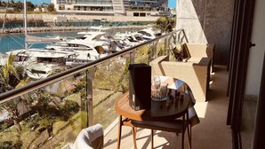 Un balcon avec vue sur un port de plaisance, un immeuble moderne et un coin repas avec une table et des chaises.