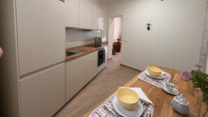 Une cuisine compacte dotée d’appareils électroménagers modernes, un coin repas avec une table en bois et une vue sur le salon.