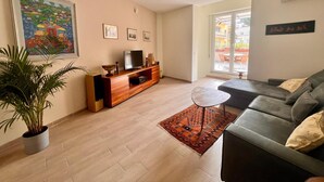 Un salon moderne avec un canapé, un téléviseur, un meuble de rangement en bois et une grande fenêtre.