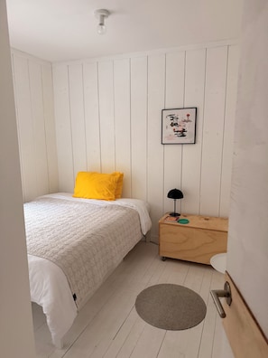 Une chambre à coucher avec un lit, une table de chevet, un tableau encadré et une porte.