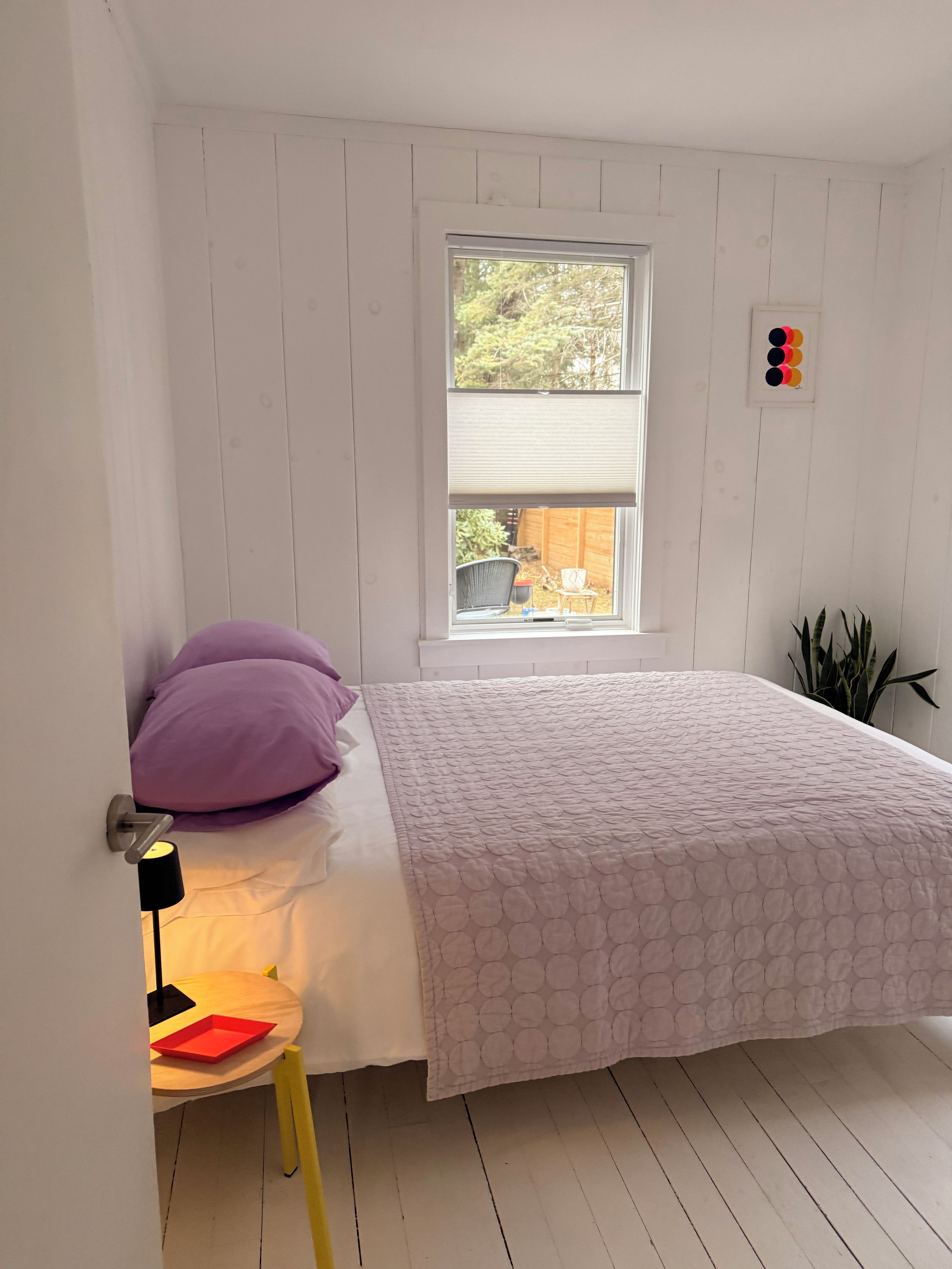 A bedroom with a bed, a window, a bedside table, and a chair.
