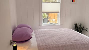A bedroom with a bed, a window, a bedside table, and a chair.