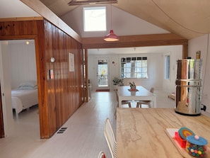Une pièce spacieuse avec un plafond en bois, une table à manger avec des chaises, un réfrigérateur et une fenêtre donnant sur des arbres.